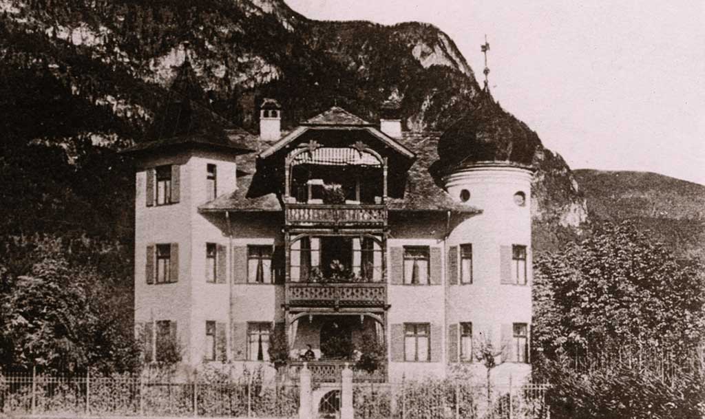 Eine historische Villa mit einzigartiger Architektur vor malerischen Alpenbergen, ideal für einen Besuch in der Region.