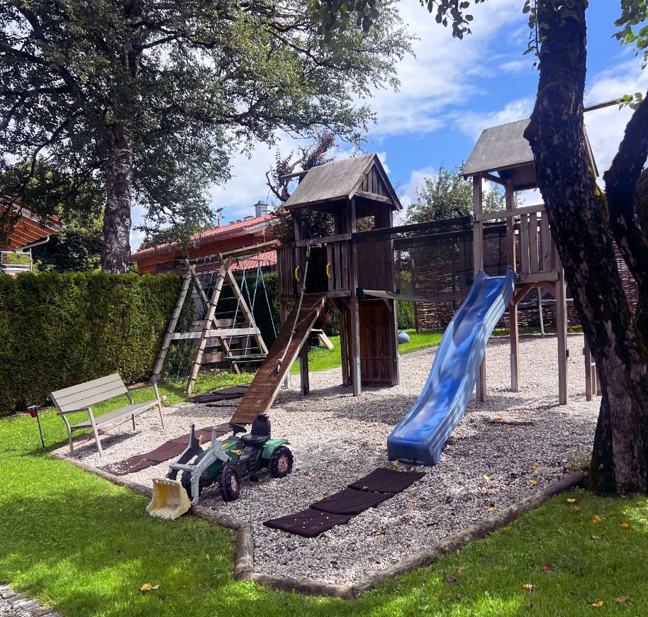Ein Spielplatz im Familienhotel mit einer Rutsche, Schaukeln und einem kleinen Traktor, ideal für den Familienurlaub.