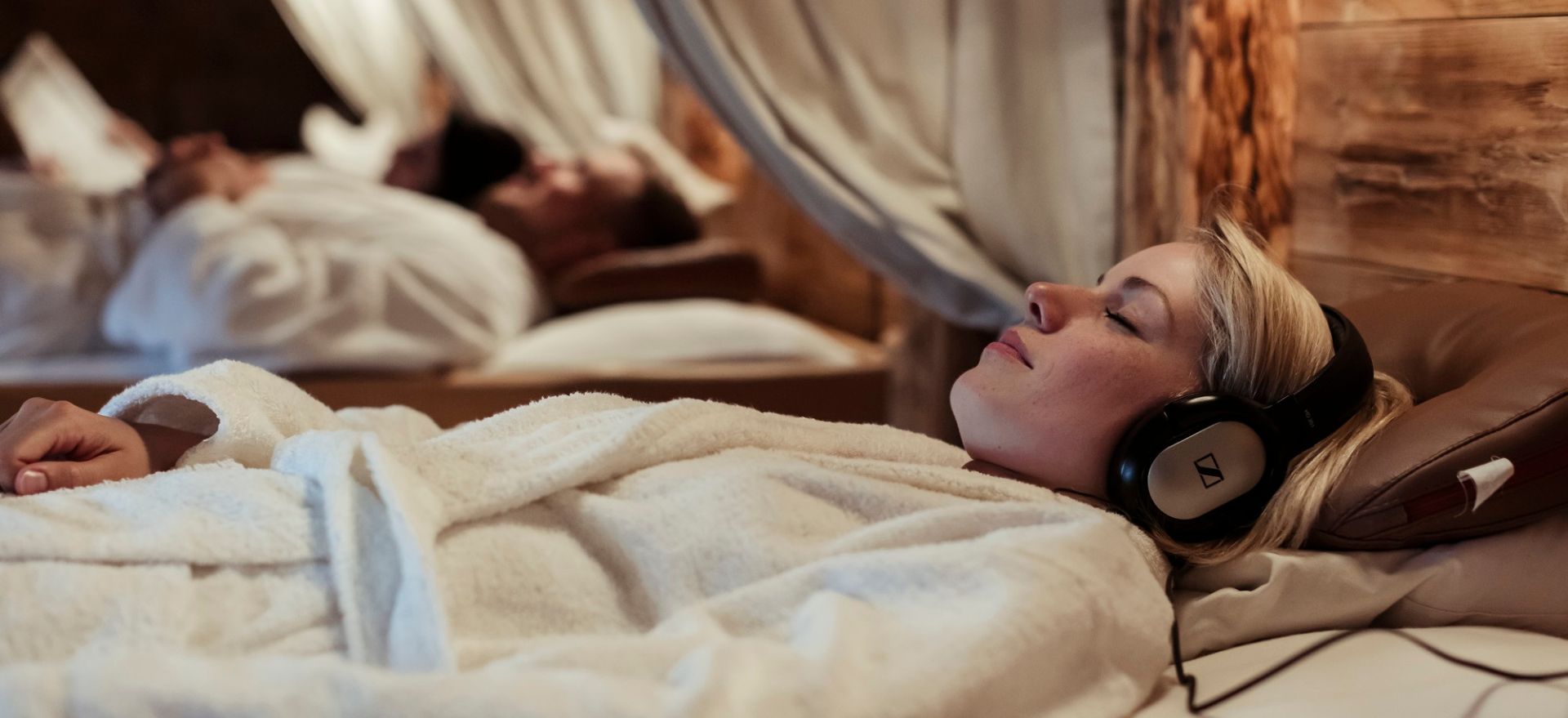 Eine Frau in einem Bademantel genießt entspannte Momente im Hotel, während sie Kopfhörer trägt und hilft dem Stress beim Wellnessurlaub zu entfliehen.