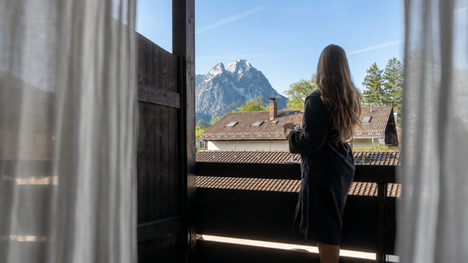 Eine Frau steht entspannt auf dem Balkon eines Familienhotels und blickt auf die beeindruckenden Berge in der Umgebung.