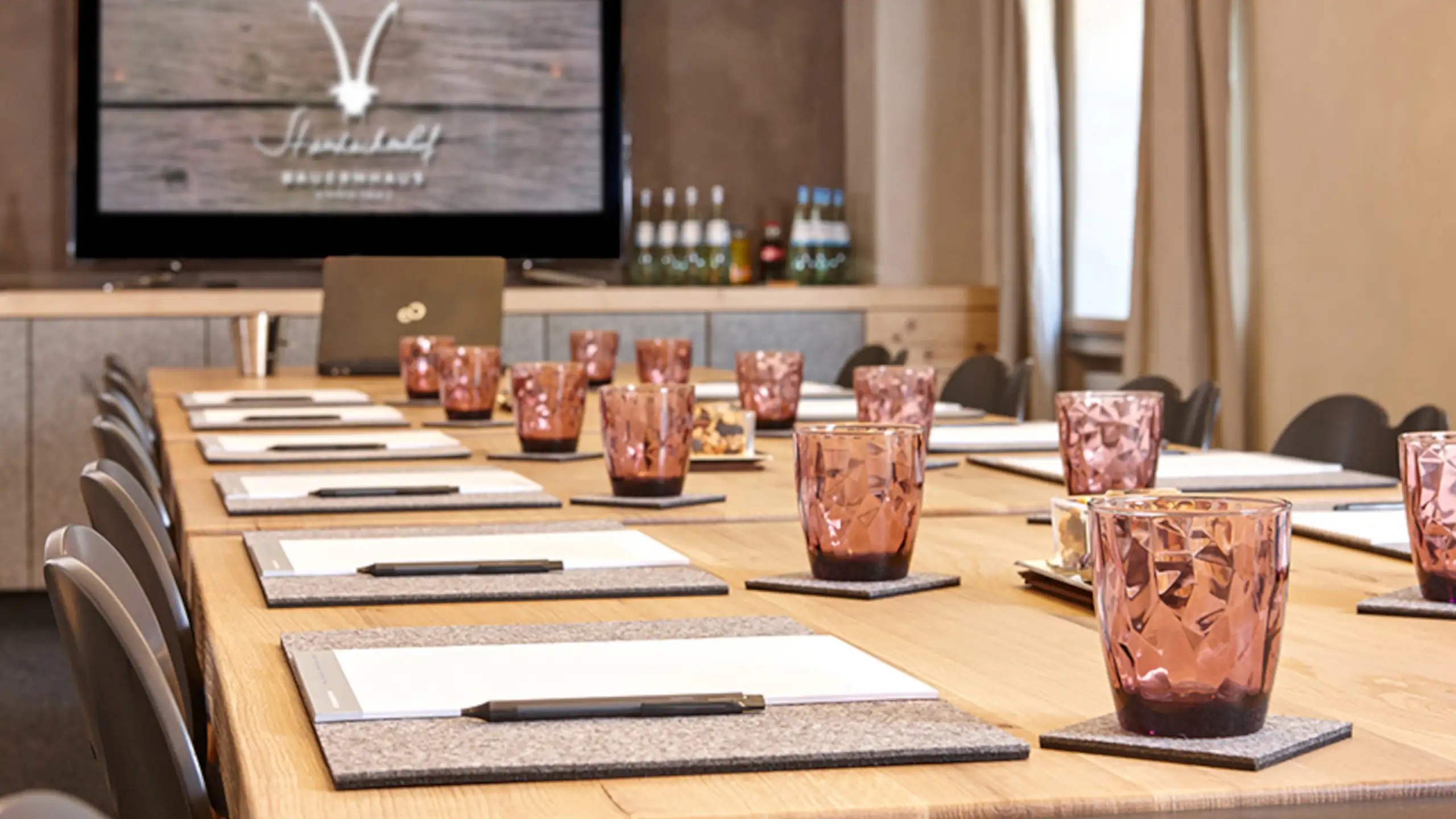 Der Tagungsraum im Hotel, ausgestattet mit einem großen Tisch, rosa Gläsern und Notizmaterial, ideal für Meetings im Familienurlaub.